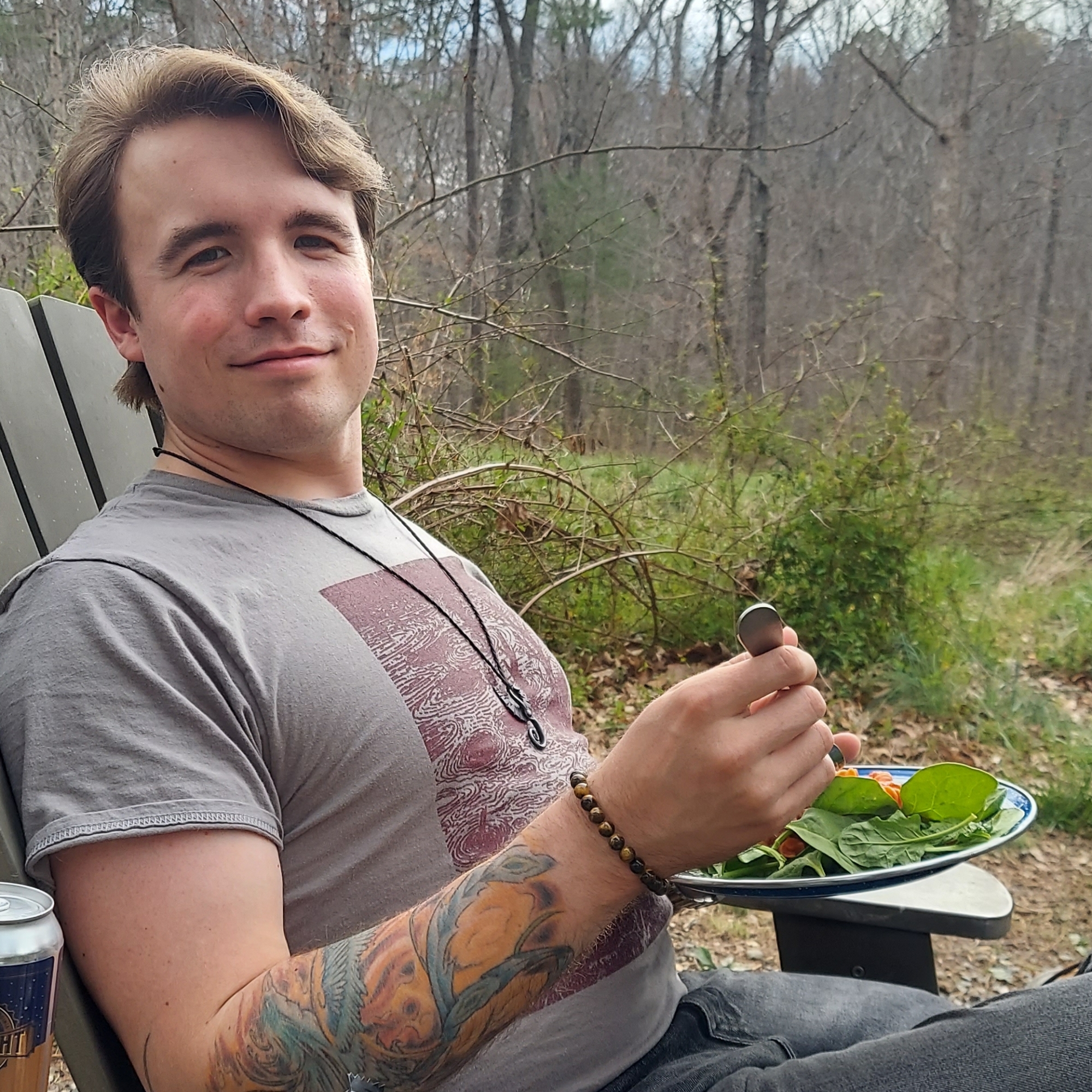 J's partner sitting outdoors, eating a plate of pasta and salad.